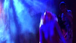 blonde woman gives a lapdance on a public stage with friends watching.